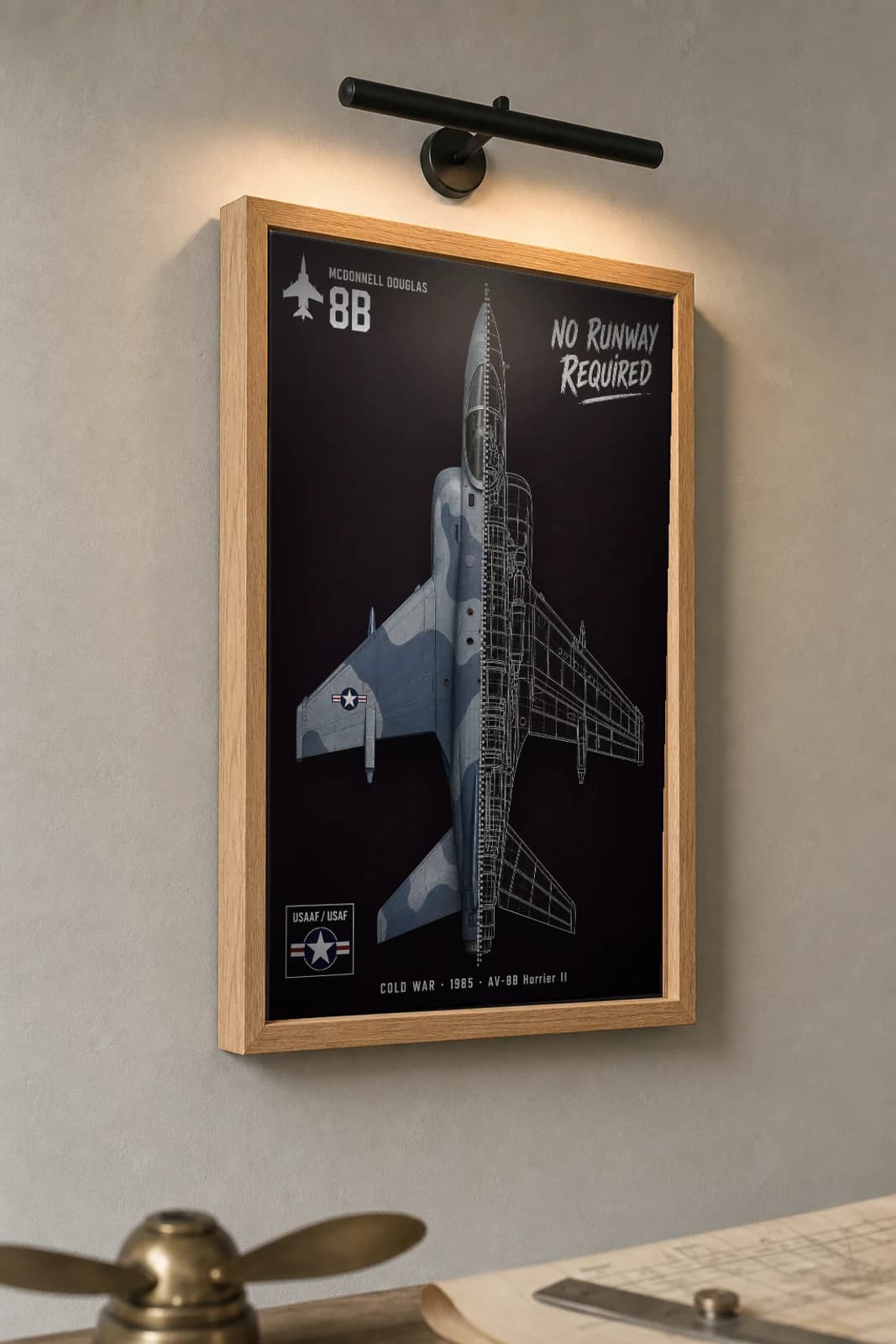 AV-8B Harrier II Cutaway Poster — AV-8B Harrier II Cold War Split-View Blueprint Print — the framed print shown at a three-quarter angle on a styled gallery wall in a natural-oak frame