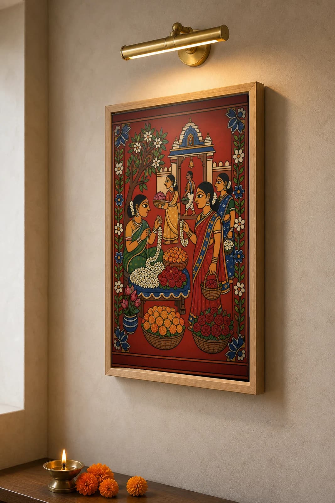 Poola Market Cheriyal Fusion Print — A Morning Flower Seller Stringing Jasmine at a Temple Gate, Nakashi Folk Grammar on a Vermilion Ground — the framed print shown at a three-quarter angle on a styled gallery wall in a natural-oak frame