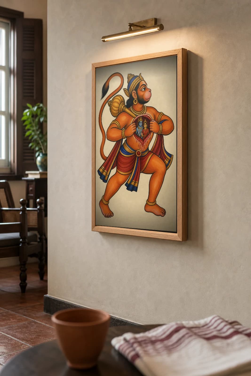 Hanuman Kalighat Print — the devoted monkey-god parting his chest to reveal Rama and Sita within, mace at his shoulder, devotional Bengal patua brush, hand-numbered collector edition — the framed print shown at a three-quarter angle on a styled gallery wall in a natural-oak frame