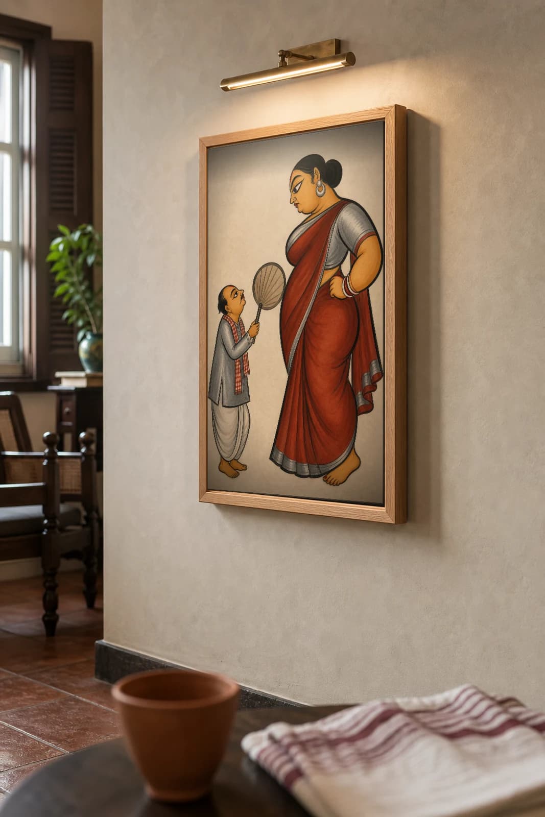 Joru Ka Ghulam Kalighat Print — the tiny henpecked husband fanning his towering wife, 19th-century Bengal patua satire of the inverted household, hand-numbered collector edition — the framed print shown at a three-quarter angle on a styled gallery wall in a natural-oak frame