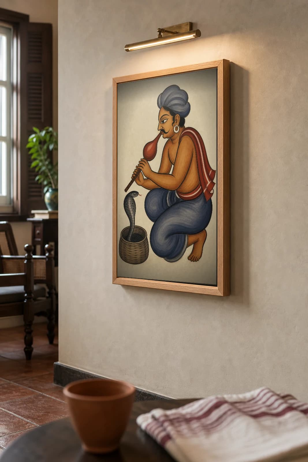 The Snake Charmer — Kalighat-style art print of a been-player coaxing a cobra from its basket, Bengal patua brush · collector edition · framed A2 — the framed print shown at a three-quarter angle on a styled gallery wall in a natural-oak frame