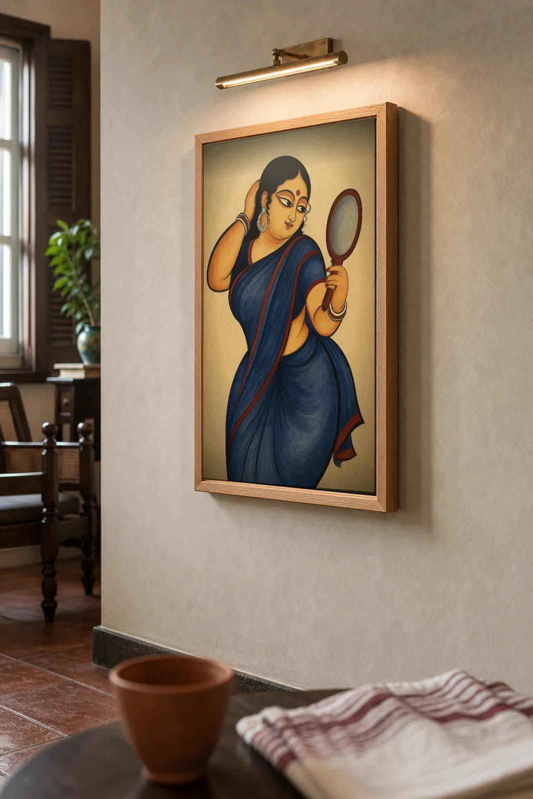 Bibi at Her Mirror — Kalighat-style art print of a woman at her toilette with a hand mirror, Bengal patua brush · collector edition · framed A2 — the framed print shown at a three-quarter angle on a styled gallery wall in a natural-oak frame