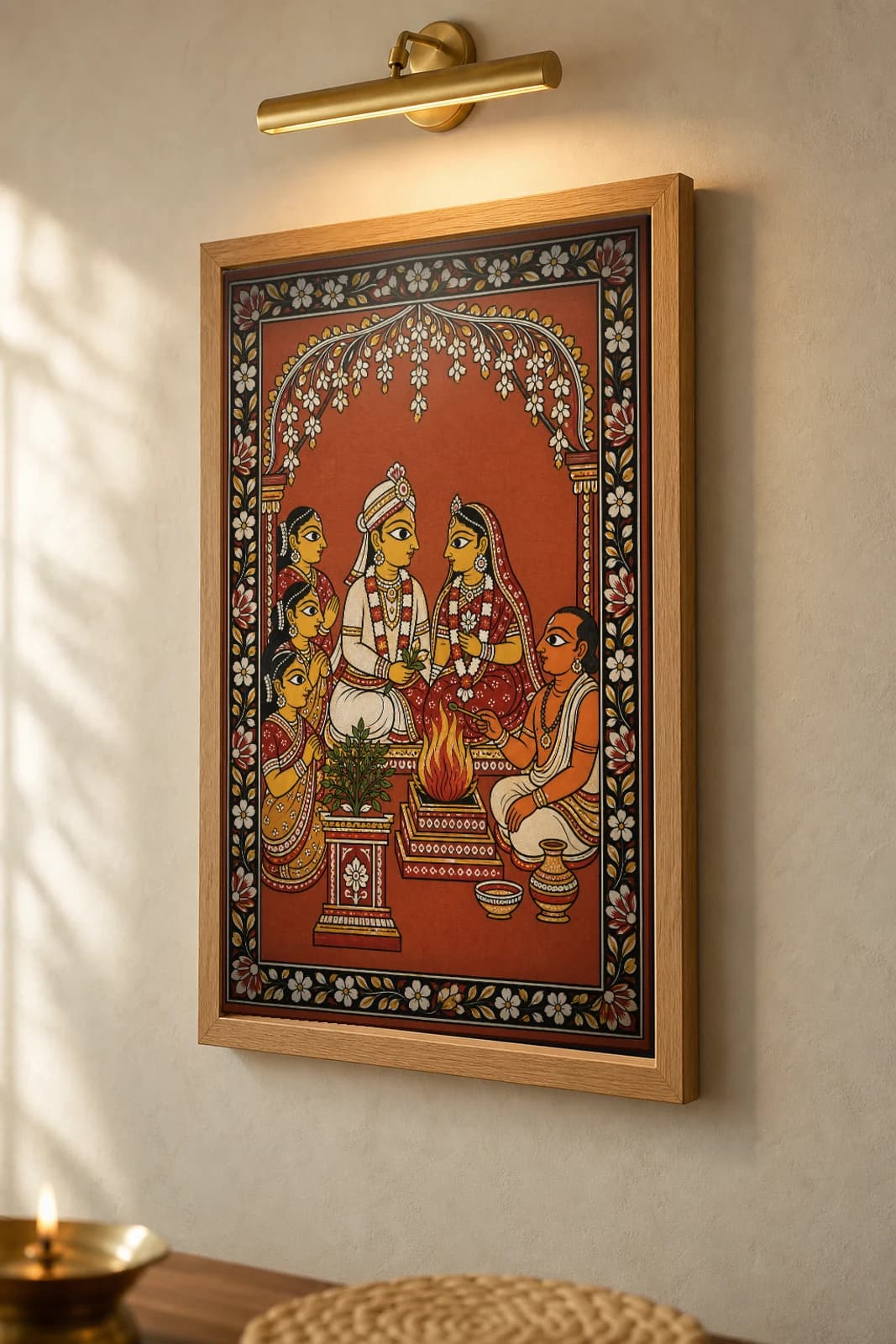 Tulasi Wedding Pattachitra Print — a courtyard marriage around the sacred fire with priest, sakhis and tulasi in patta line · collector edition A2 · contemporary fusion — the framed print shown at a three-quarter angle on a styled gallery wall in a natural-oak frame