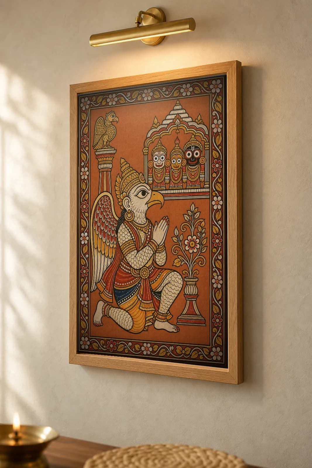 Garuda Stambha Pattachitra Print — the eagle-mount kneeling in devotion before the Jagannath triad · collector edition A2 · classical Odisha cloth-painting grammar — the framed print shown at a three-quarter angle on a styled gallery wall in a natural-oak frame