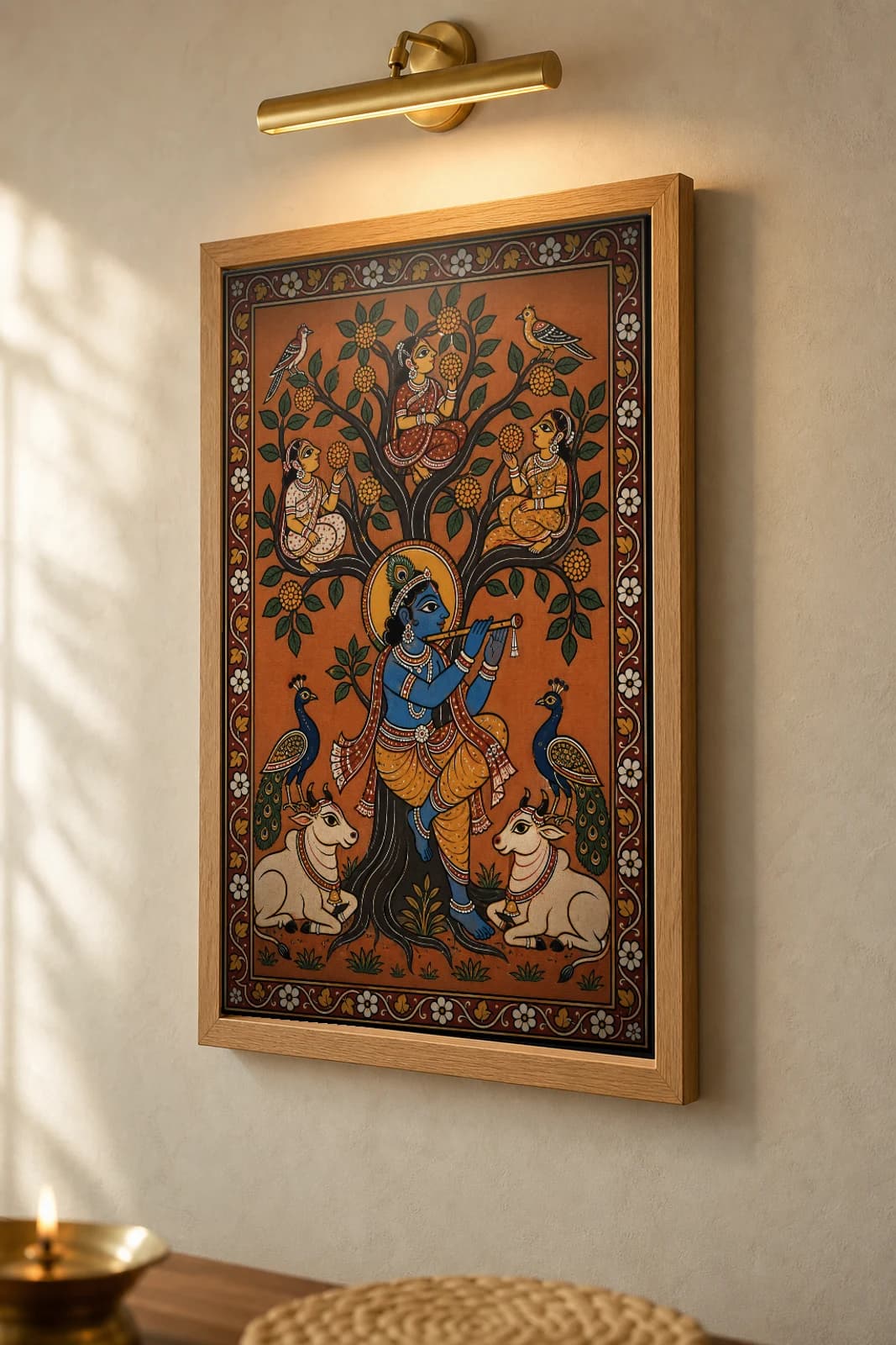 Kadamba Tree Pattachitra Print — flute-playing Krishna beneath the kadamba with gopis, peacocks and cows · collector edition A2 · classical Odisha cloth-painting grammar — the framed print shown at a three-quarter angle on a styled gallery wall in a natural-oak frame