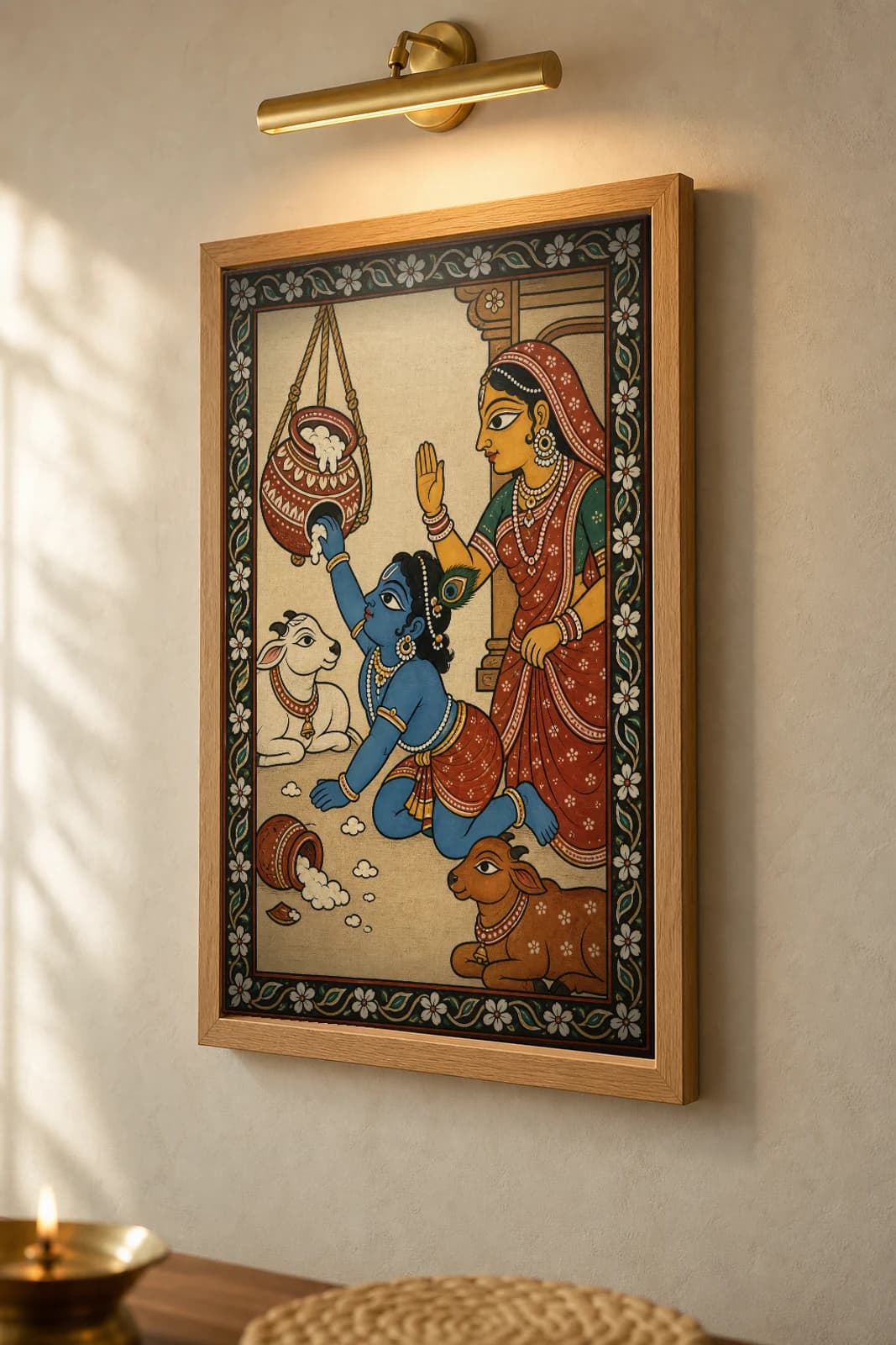 Makhan Chor Pattachitra Print — child Krishna and the butter pot in Odisha cloth-painting grammar · collector A2 · Krishna leela — the framed print shown at a three-quarter angle on a styled gallery wall in a natural-oak frame