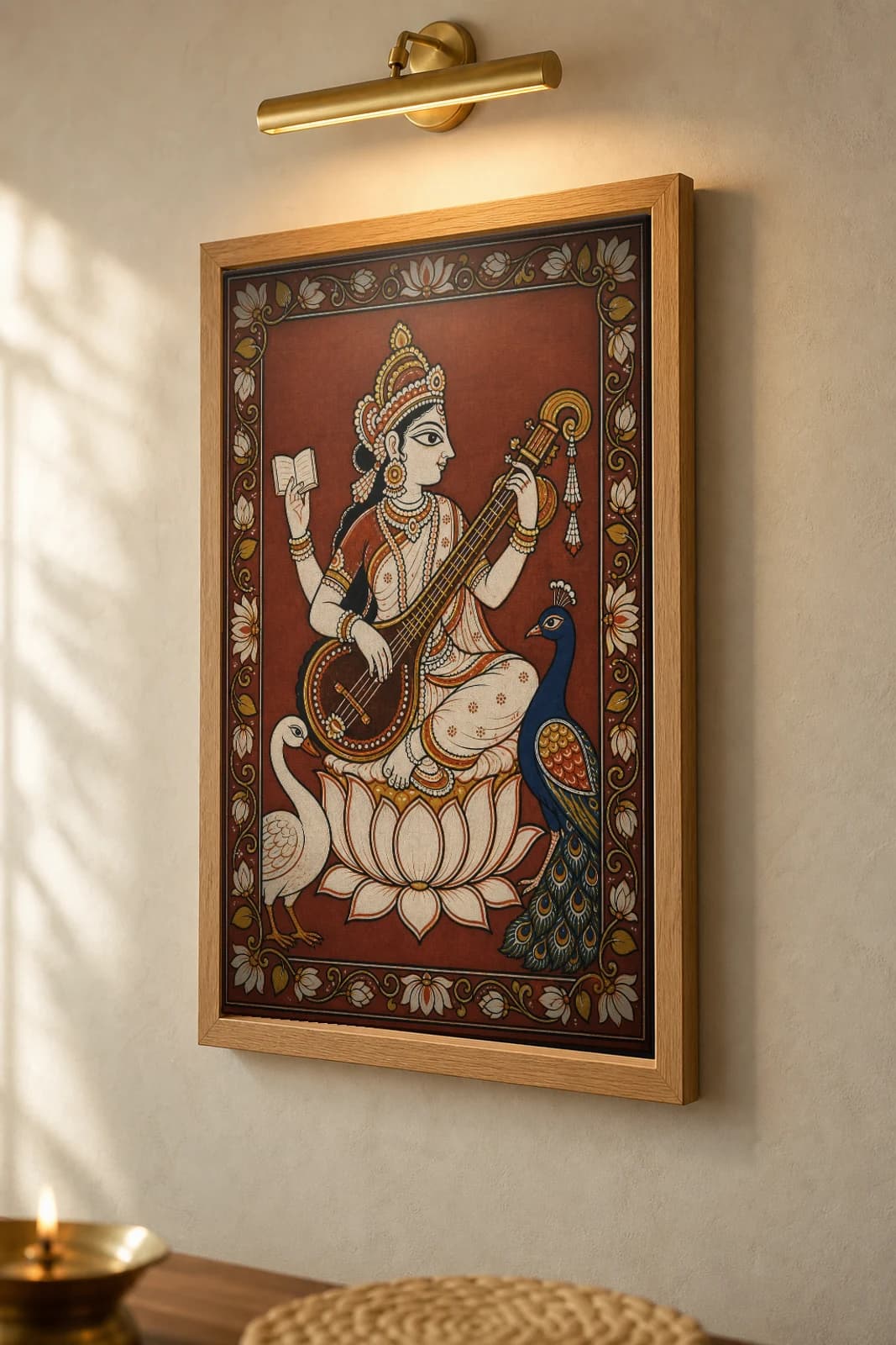 Saraswati Pattachitra Print — the goddess of learning with her veena in Odisha cloth-painting grammar · collector A2 · Devi / Shakti — the framed print shown at a three-quarter angle on a styled gallery wall in a natural-oak frame