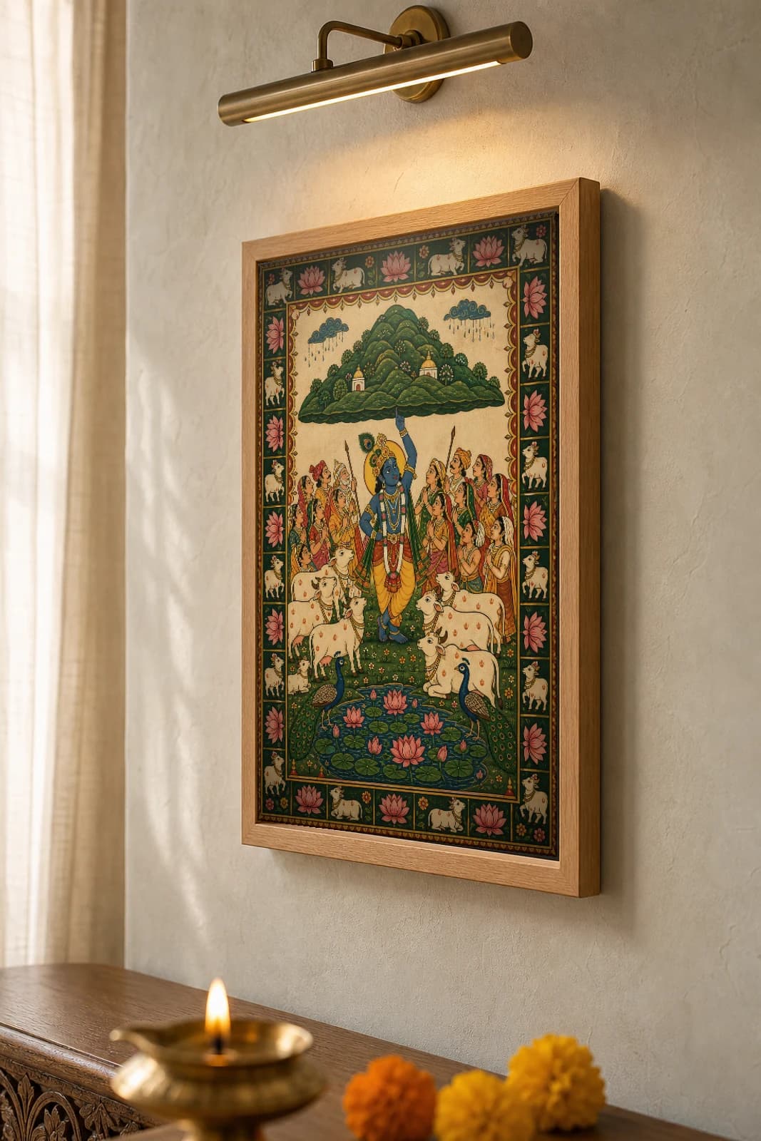 Govardhan Lila Pichwai-Style Print — Krishna lifting Mount Govardhan on one finger to shelter villagers and cows from the rain, with a lotus pond, on warm cream cloth — the framed print shown at a three-quarter angle on a styled gallery wall in a natural-oak frame
