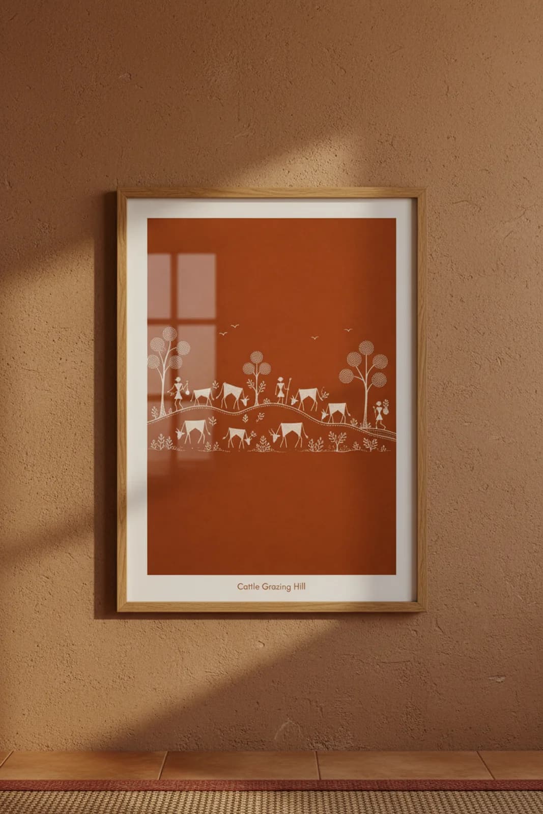 Cattle Grazing Hill Warli print in natural oak A2 frame on terracotta-ochre mud-plaster wall — rustic Indian folk art mockup