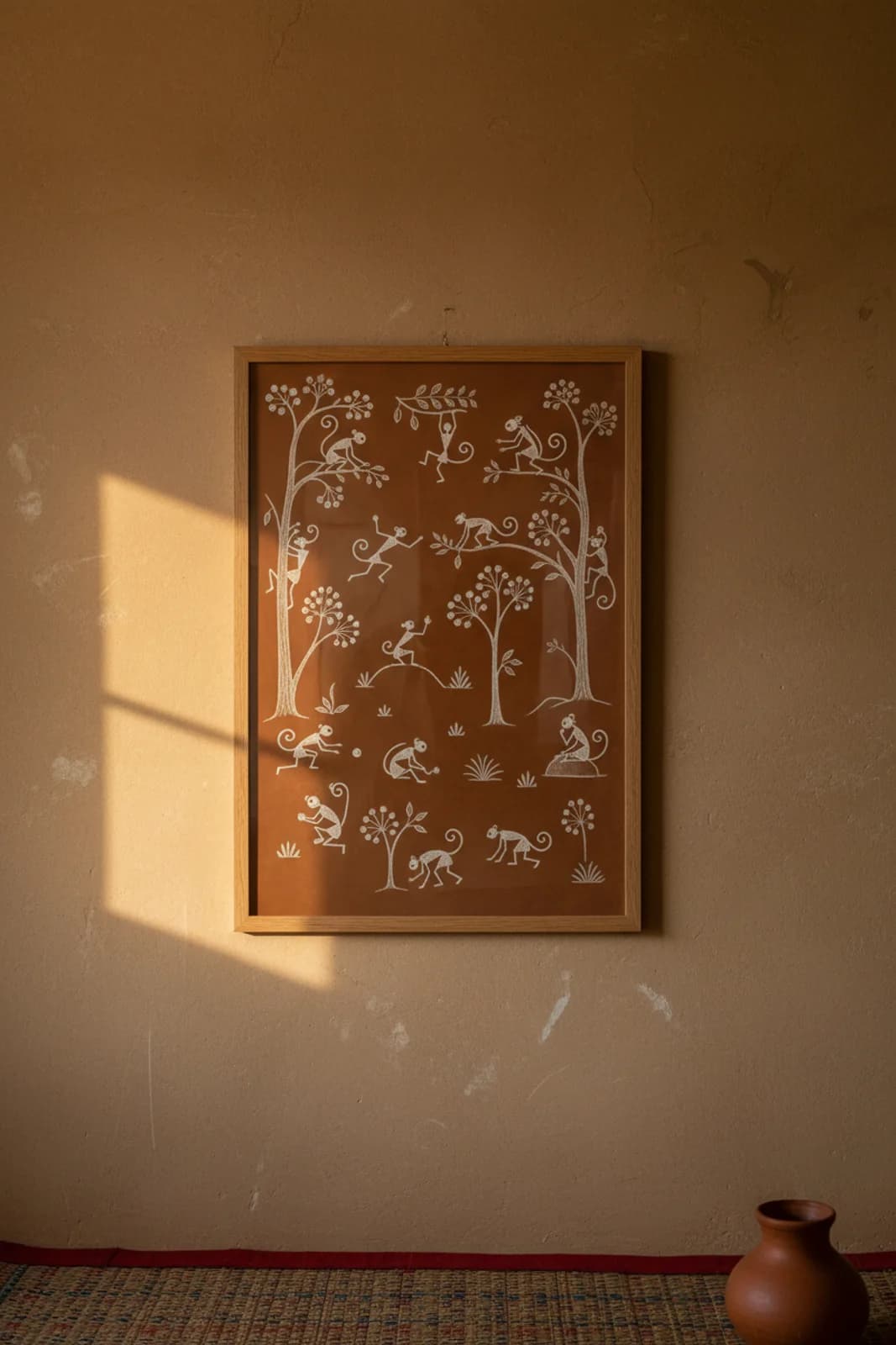 Monkey Troop Canopy Warli print in natural oak A2 frame on warm-earth-neutral mud-plaster wall — rustic Indian folk art mockup