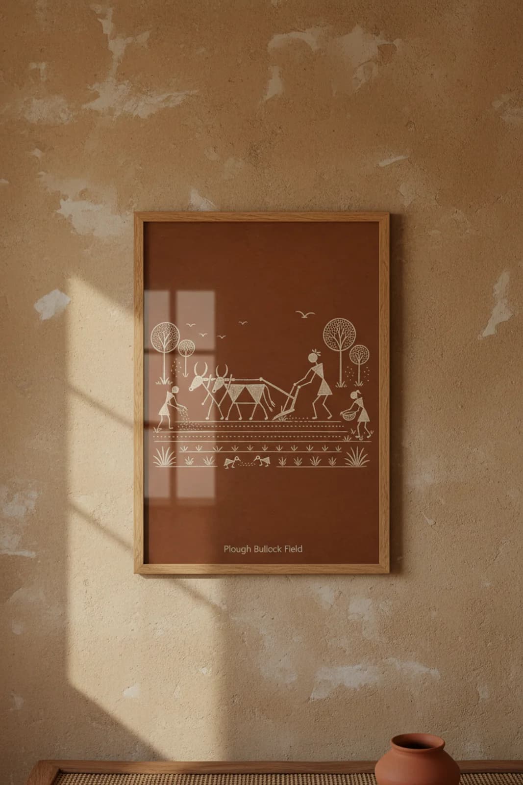 Plough Bullock Field Warli print in natural oak A2 frame on warm-earth-neutral mud-plaster wall — rustic Indian folk art mockup