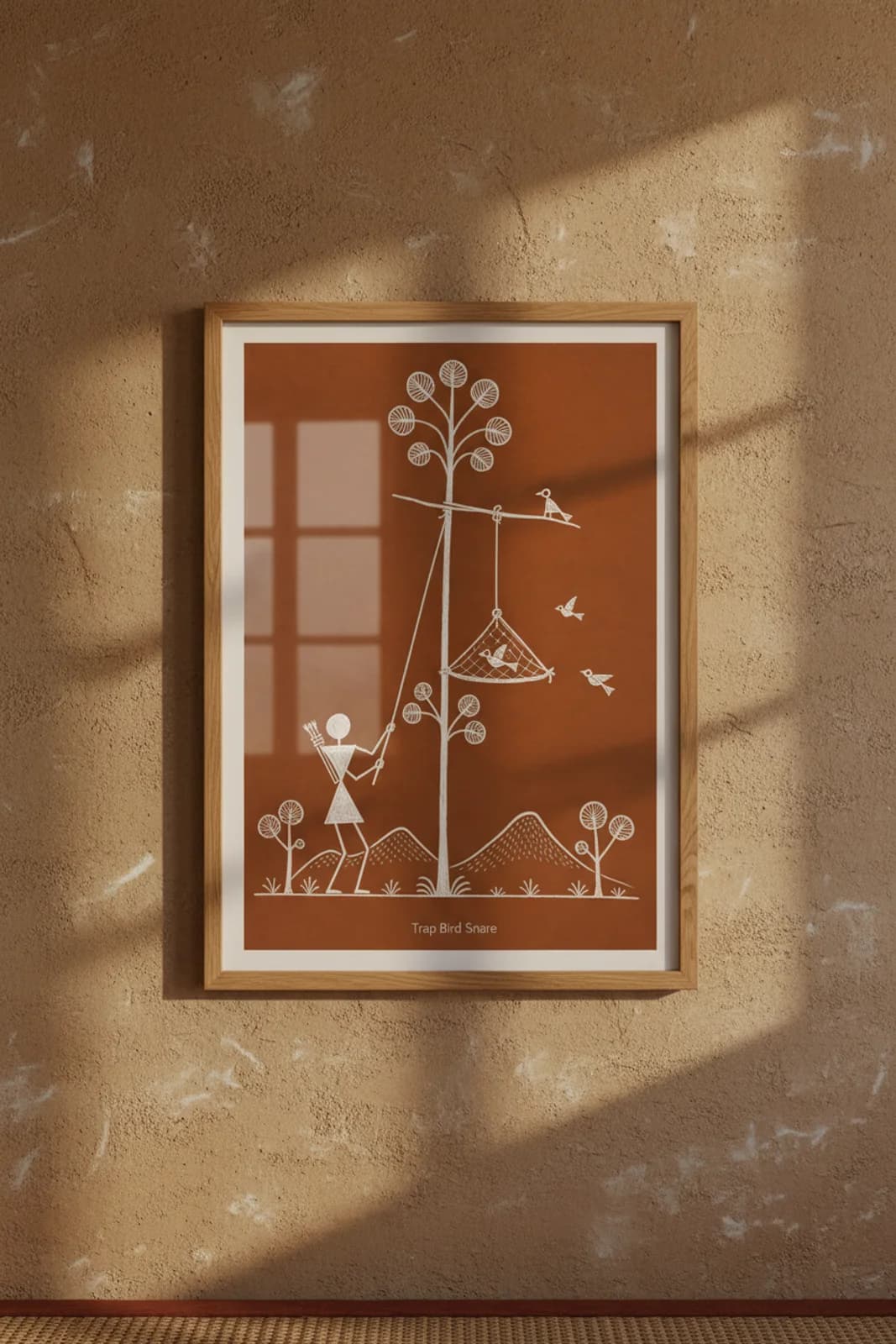 Trap Bird Snare Warli print in natural oak A2 frame on warm-earth-neutral mud-plaster wall — rustic Indian folk art mockup